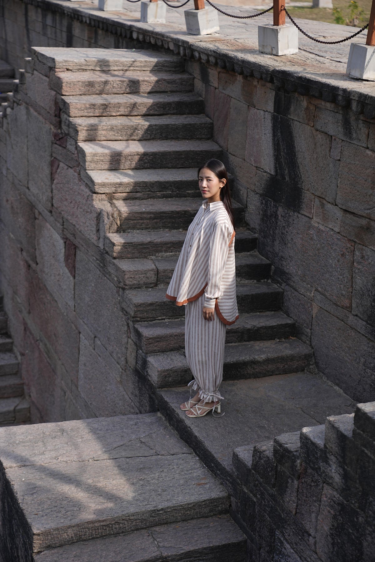 Woman wearing the Sutra Arc Stripe co-ord — a striped cotton button-down shirt with matching ruffled-hem trousers
