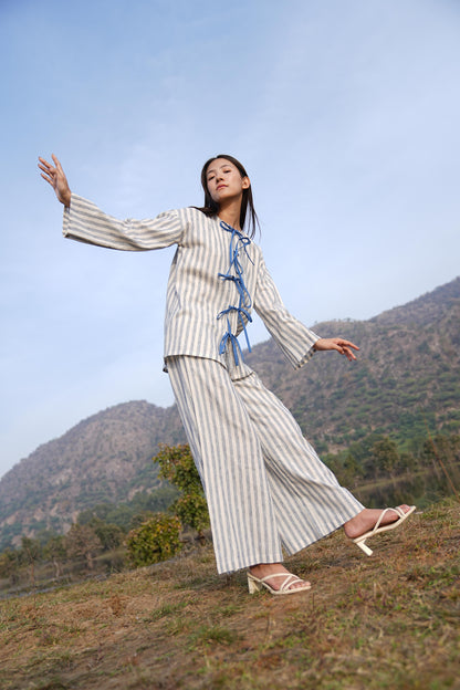 Woman wearing the Sutra Bow Stripe co-ord — an open-front striped cotton tunic tied with blue fabric ties over wide-leg trousers